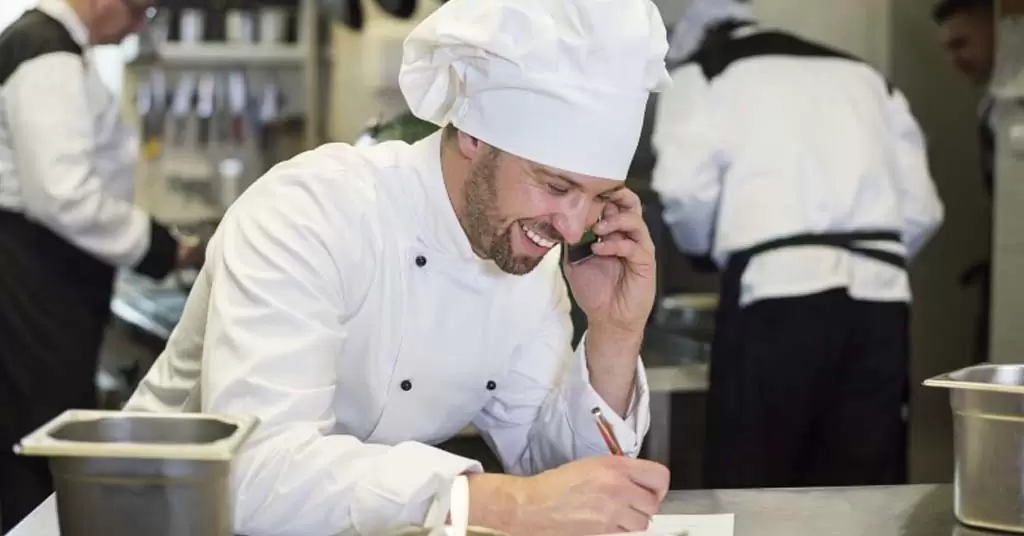 Szef kuchni rozmawia przez telefon z dostawcami, aby zaplanować dostawy do swojej kuchni.